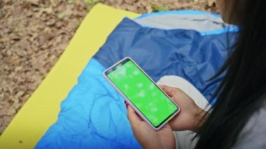 Mutlu Asyalı kadın tatilin tadını çıkarıyor, video görüşmesinde konuşuyor, telefonda film izliyor, Forest City Park 'ta çadırda dinleniyor. yaz kampı