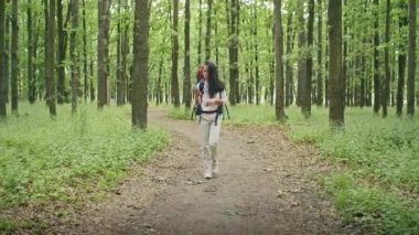 Sırt çantalı mutlu Asyalı bir kadın ormanda bir yol arıyor, telefon kullanıyor, görüntülü konuşuyor, haritaya bakıyor. yaz kampı