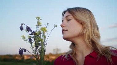 Genç bir kadın gün batımında yürüyüş sonrası dinlenmek için dağ tepelerinden çiçekler topluyor. Doğadaki diğer bir kişi, dağlarda.