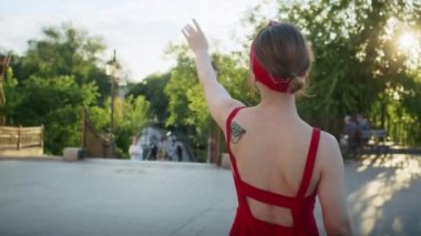 Kırmızı elbiseli mutlu kız parkta yürüyor, sokağın batan güneşinin tadını çıkarıyor, yaz yaşam tarzı.
