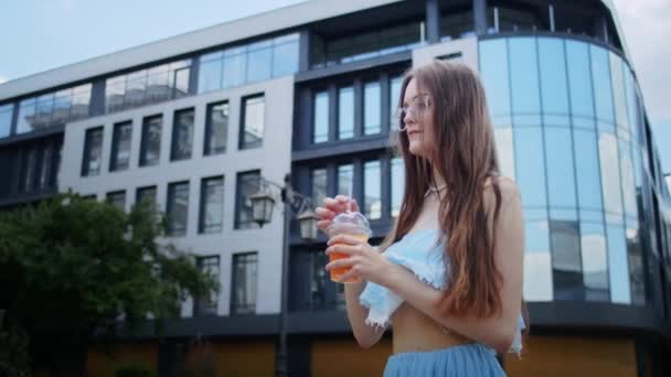 一个穿着蓝色衣服 戴着眼镜的快乐的女孩 靠着一栋大楼的背景 在街上喝着鸡尾酒 过着悠闲的生活 夏天过得很开心 — 图库视频影像