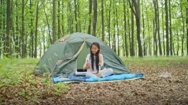 Mutlu Asyalı kadın tatilin tadını çıkarıyor, video görüşmesinde konuşuyor, telefonda film izliyor, Forest City Park 'ta çadırda dinleniyor. yaz kampı