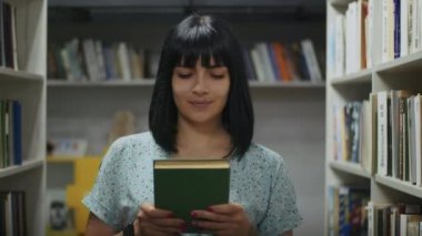 Mutlu ve hayalperest kadın kütüphanede kitap okuyor, raftan kitap seçiyor. Öğrenciler için kütüphanede öğrenim.