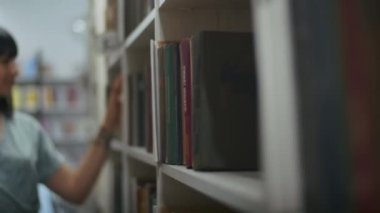 Mutlu ve hayalperest kadın kütüphanede kitap okuyor, raftan kitap seçiyor. Öğrenciler için kütüphanede öğrenim.