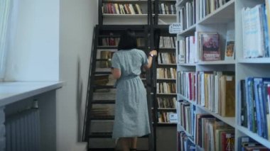 Mutlu ve hayalperest kadın kütüphanede kitap okuyor, raftan kitap seçiyor. Öğrenciler için kütüphanede öğrenim.