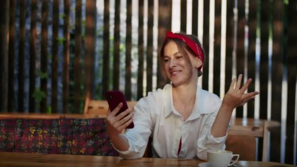 幸せな女の子は電話やビデオを経由してビデオ通話で話して 通りのカフェで 簡単なライフスタイルと夏の時間の楽しみ — ストック動画
