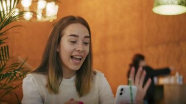 Kafede çay içip telefonda ya da görüntülü konuşma yapan neşeli bir kız. İyi eğlenceler.