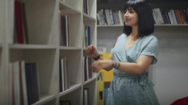 Mutlu ve hayalperest kadın kütüphanede kitap okuyor, raftan kitap seçiyor. Öğrenciler için kütüphanede öğrenim.