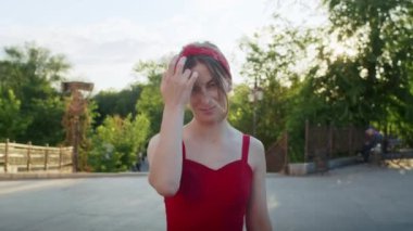 Kırmızı elbiseli mutlu kız parkta yürüyor, sokağın batan güneşinin tadını çıkarıyor, yaz yaşam tarzı.