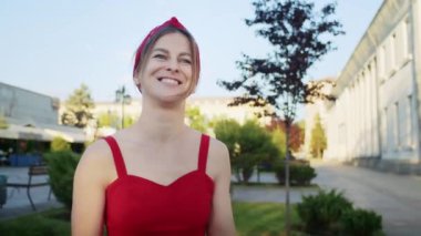 Kırmızı elbiseli mutlu kız parkta yürüyor, sokağın batan güneşinin tadını çıkarıyor, yaz yaşam tarzı.