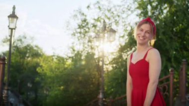 Kırmızı elbiseli mutlu kız parkta yürüyor, sokağın batan güneşinin tadını çıkarıyor, yaz yaşam tarzı.