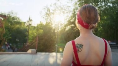 Kırmızı elbiseli mutlu kız parkta yürüyor, sokağın batan güneşinin tadını çıkarıyor, yaz yaşam tarzı.