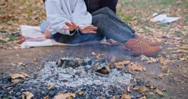 a happy girl, together with her boyfriend, sits hugging by the fire, warms her hands, on a cold autumn day. family vacation young family outdoors.