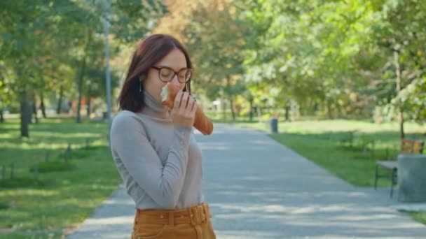 若い幸せな女性はシティパークでバゲットを食べる 女の子は一緒に楽しんでる 若者や静けさ夏や秋の公園 — ストック動画