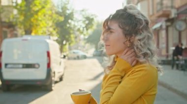 Rahatlamış, gülümseyen, kırmızı kahve fincanı olan, güneşli bir günün tadını çıkaran bir kadın.