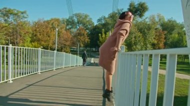 Gözlüklü genç mutlu kadın şehir parkında köprü boyunca yürüyor. sonbahar yaz dönemi
