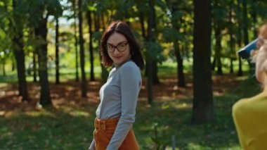 Şehir parkının arka planında poz veren mutlu genç kız arkadaşı fotoğrafçıya. gençlik ve güzellik