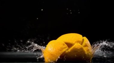 Slo-motion lemon falling into wedges against black drop.
