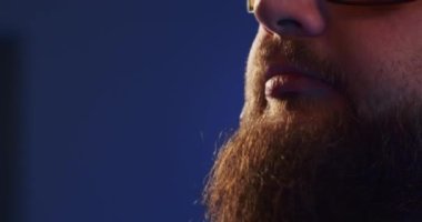 Close-up of a European podcast blogger smiling while broadcasting his live audio podcast in a studio using a microphone and headphones. Male radio host with glasses, podcast host or interviewer.