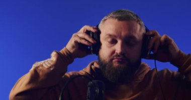 Close-up of a European podcast blogger smiling while broadcasting his live audio podcast in a studio using a microphone and headphones. Male radio host with glasses, podcast host or interviewer.