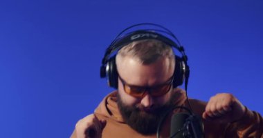 Close-up of a European podcast blogger smiling while broadcasting his live audio podcast in a studio using a microphone and headphones. Male radio host with glasses, podcast host or interviewer.