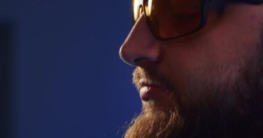 Close-up of a European podcast blogger smiling while broadcasting his live audio podcast in a studio using a microphone and headphones. Male radio host with glasses, podcast host or interviewer.