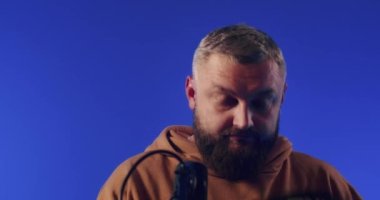 Close-up of a European podcast blogger smiling while broadcasting his live audio podcast in a studio using a microphone and headphones. Male radio host with glasses, podcast host or interviewer.