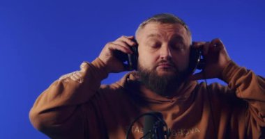 Close-up of a European podcast blogger smiling while broadcasting his live audio podcast in a studio using a microphone and headphones. Male radio host with glasses, podcast host or interviewer.