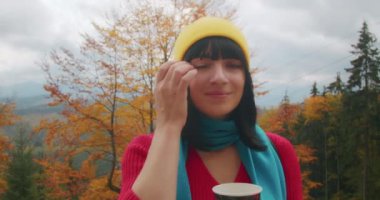 Dağlarda genç bir kadın gezgin sıcak bir içecekle ısınıyor. Sonbahar maceraları. Z kuşağı yolculuğu.