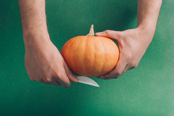 Erkeklerin elinde taze balkabağı ve bıçakla yaratıcı bir Cadılar Bayramı fikri. Asgari kesim ve zanaat konsepti, tatil sezonu estetik görselleştirme. Huysuz koyu yeşil arkaplan.