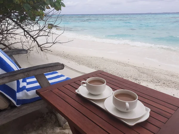Dwie filiżanki kawy na drewnianym stole. Malediwy, plaża z białym piaskiem w pobliżu błękitnego oceanu. — Zdjęcie stockowe