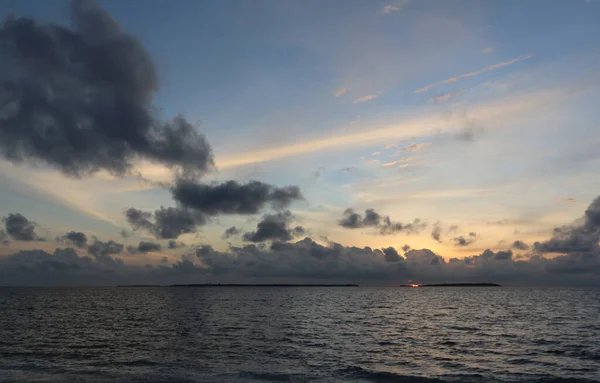 Sunset wiht blue sky and dark clouds in the ocean. Small Maldivian islands on the horizon. — Stock Photo, Image