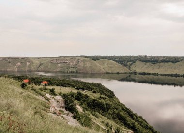 Sakin suyu olan büyük bir nehrin kıyısındaki evler. Bakota Körfezi kırsal manzarası. Dinyester nehri manzarası, Ukrayna. Sakin bej renklerle yaz günü. Yüksek kıyılar, yeşil tepeler, panoramik nehir.