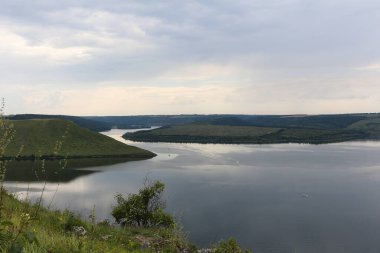 A calm smooth water view. The landscape of Bakota Bay on the Dniester river, Ukraine. The banks of a large river. High banks, summer green hills.