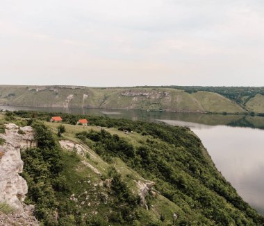 Dniester Nehri, Ukrayna. Bakota Körfezi kırsal manzarası. Sakin suyu olan büyük bir nehrin yüksek kayalık kıyılarındaki evler. Yüksek bankalar, yeşil tepeler, panoramik nehir. Durgun bej renklerde yaz manzarası.