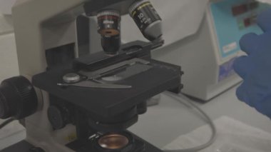 Eldivenli bilim adamı mikroskop altında örnek analiz ediyor.