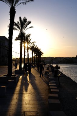 seafront of Brindisi at sunset. palms and people in backlight