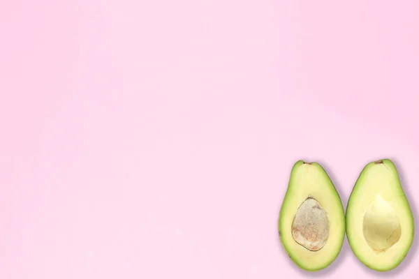 Pembe arka planda tohumlu ve tohumsuz iki buçuk avokado. Üst görünüm.