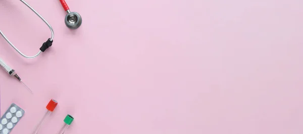 Kırmızı stetoskop, şırınga, ampuller ve pembe arka planda beyaz haplar. Tıp konsepti. Sancak boyutu.