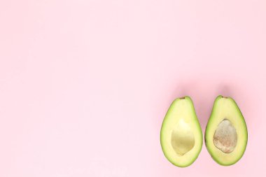 Pembe arka planda tohumlu ve tohumsuz iki buçuk avokado. Üst görünüm.