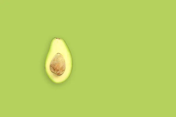 Eine Hälfte Avocado mit Samen auf grünem Hintergrund. Ansicht von oben. — Stockfoto