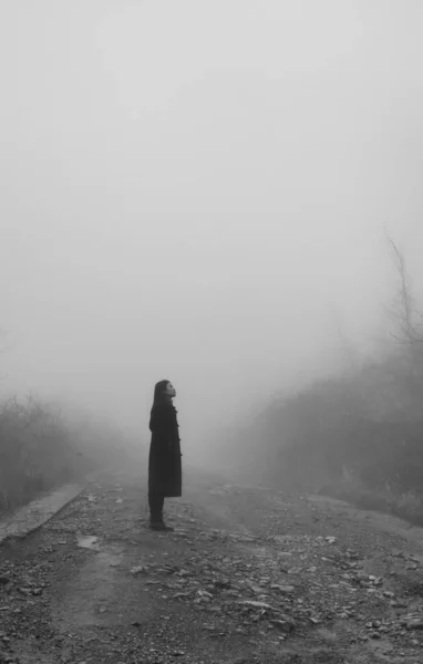 young woman in black dress with fog on the background of the mountain