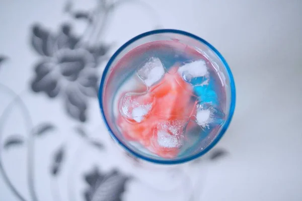 a glass of water with ice cream and a red berries on a blue background