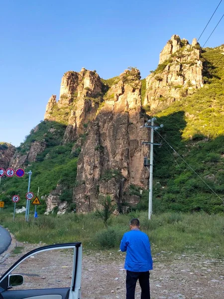 a man in a green jacket and a backpack on the road in the mountains