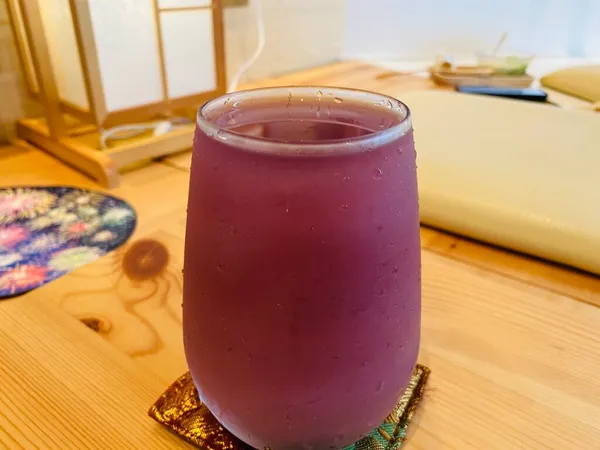 a glass of red juice with a knife and a spoon on a wooden table