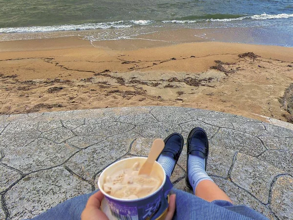 woman legs on the beach with a cup of coffee on the shore