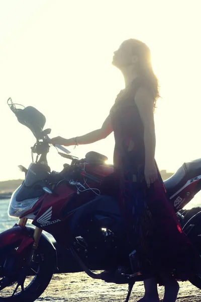 young woman with a motorcycle on the background of the sunset