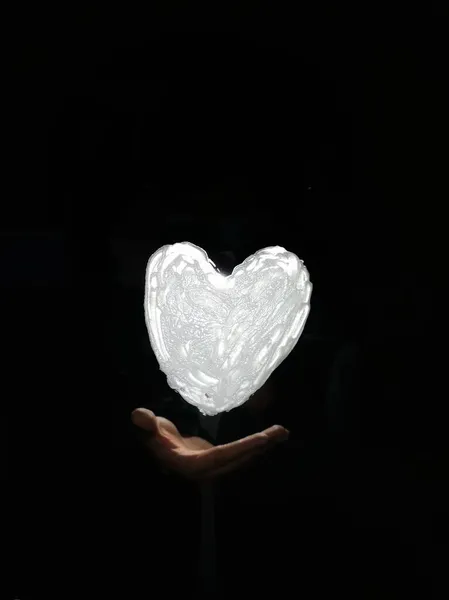 heart shaped hand holding a black and white hearts on a dark background