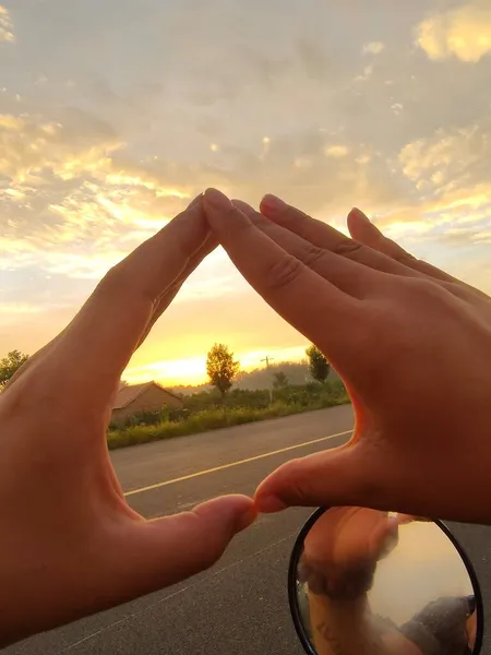 hand holding a heart shaped sign on the background of the sunset