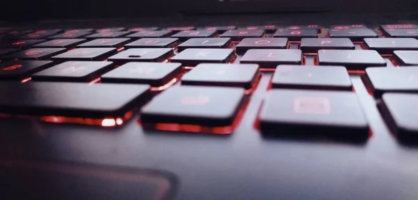 close up of a laptop keyboard with a red computer mouse on a black background